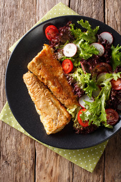 fried fish hake with salad from tomato, radish and lettuce close-up. Vertical top view