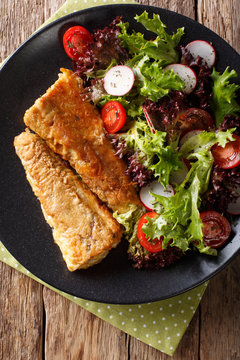 Healthy lunch: fried hake with tomato, radish and lettuce salad close-up. Vertical top view