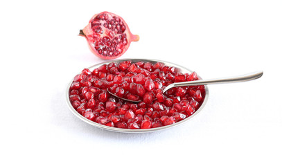 Pomegranate seeds scoop in a steel spoon a plate with the same seeds.