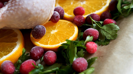 Closeup view of Whole Raw Chicken with Fresh parsley Cranberries and Orange Slices on baking tray tin prepared for roasting in oven