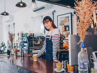 Young asian woman portrait of barista, coffee shop owner standing behind the counter.