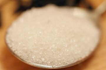 Sugar sand on a silver spoon and on a wooden background