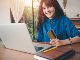 Asian woman handholds a credit card and using a laptop computer to shopping online at the table in coffee shop.