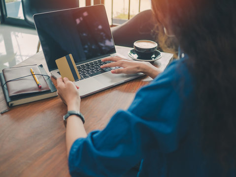 Asian Woman Hand Holds A Credit Card And Using A Laptop Computer To Shopping Online At The Table In Coffee Shop.