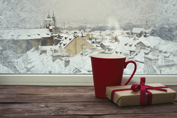 A frozen window and a red cup and a gift on the windowsill with a beautiful view of winter Prague