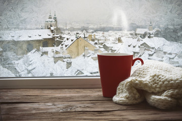 Frozen window and a red cup with a scarf on the windowsill with a beautiful view of winter Prague