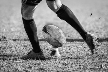 Legs of rugby player kicking ball
