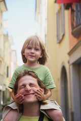 Happy faces of a man and a child sitting on his shoulders. Walk around the city.