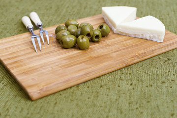 Green olives and goat cheese on a wooden background.