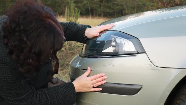 Woman inspects car damage after an accident