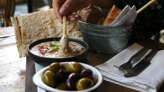 Closeup Hand Dips Bread Stick In Healthy Hummus With Olives And Fresh Pita Bread