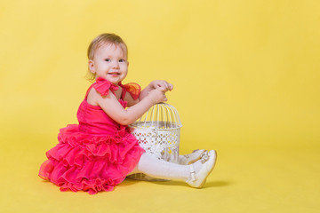 Girl toddler in a pink dress on a yellow background sits on the floor and looking at the camera