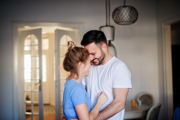 Romantic playful young love couple standing hugged and looking each other at home in pajamas.