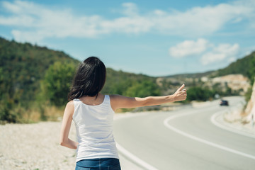 Beautiful young female hitchhiking at the country road. Hitchhiking tourism concept.