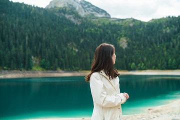 Fototapeta premium Young beautiful woman hiking in a national park, azure lake water and high mountain on the background. Black Lake, Montenegro