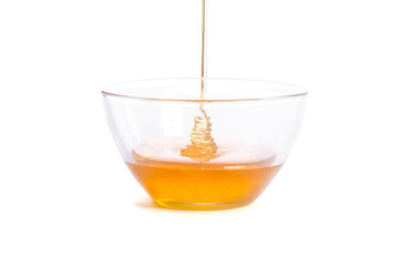 Pouring honey into a glass bowl on a white background