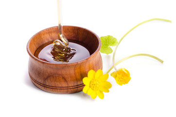 pouring honey in the wooden bowl with yellow flowers isolated on white background