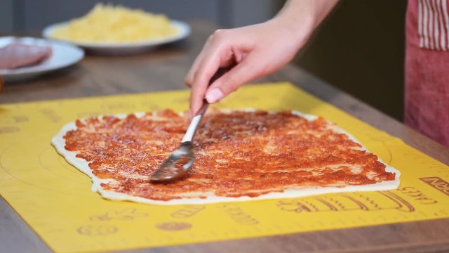 Putting tomato sauce on top of the pizza