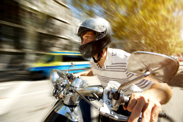 Man riding a scooter at speed on the road with blurred background.