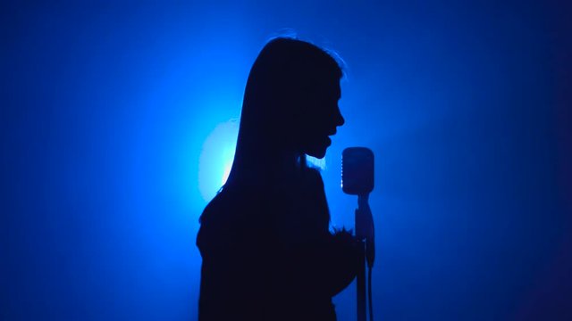 Girl sings songs for the clip. Smoke background. Silhouette. Side view
