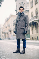 Young stylish man in warm gray coat and leather gloves walking down the street. Street style.