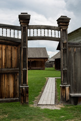 Old wooden gate with ornaments and a small roof with wickets on either side of them. Photos near