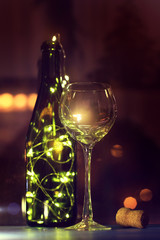 romantic atmosphere for pastime/ bottle full of glowing lights and glass of wine on the table in the evening