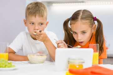 Kids eat breakfast while watching a movie on a tablet pc