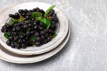 Chokeberry in silver metal bowl on grey background. Aronia berry with leaf. Top view. Copy space.