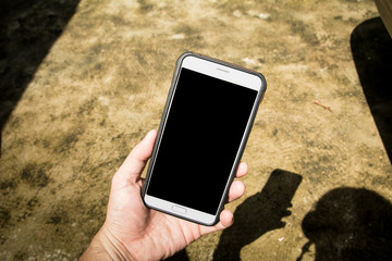 Hand holding mobile phone isolated on cement background