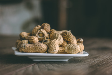 Roasted peanuts on a white saucer on top of a wooden table