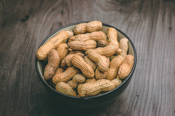 Roasted peanuts inside a black bowl on top of a wooden table