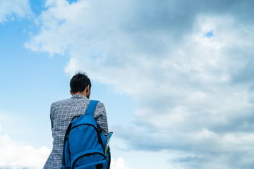 Young man with backpack  standing alone on a background of cloudy sky