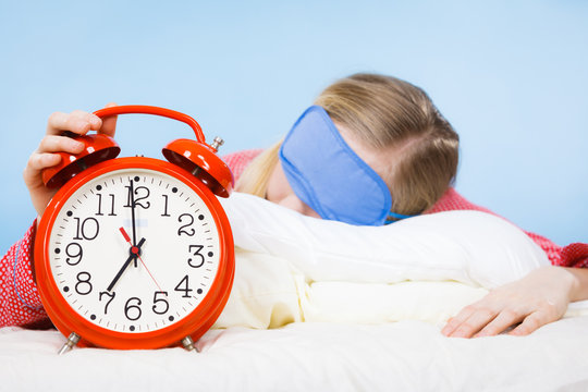 Sleeping woman wearing pajamas holding clock