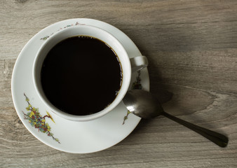 a little white cup with black coffee on saucer with spoon on wooden table