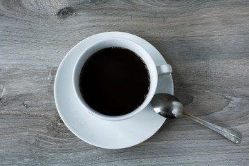 a little white cup with black coffee on saucer with spoon on wooden table