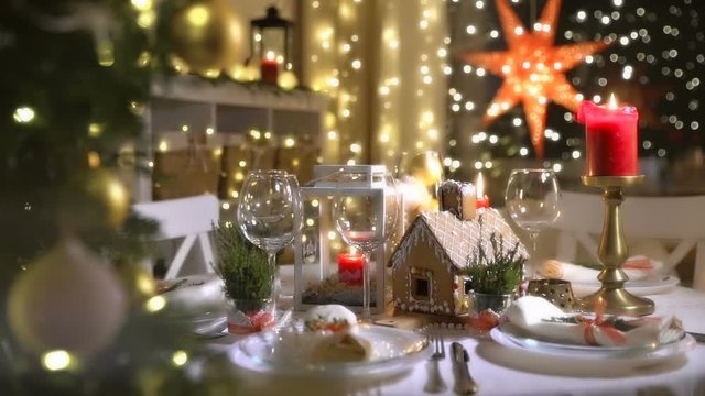 Homemade Christmas Gingerbread House on a celebration table. Christmas tree lights, candles, and festive serving.