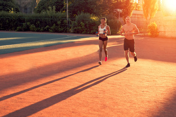 The guy and the girl at the stadium are doing sports, running