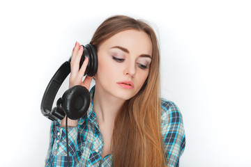 Headshot of a young adorable blonde woman in blue plaid shirt enjoying listening music to big professional dj headphones.