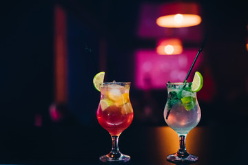 two glasses with fruit cocktails with lime, orange and mint and straws at party on bar