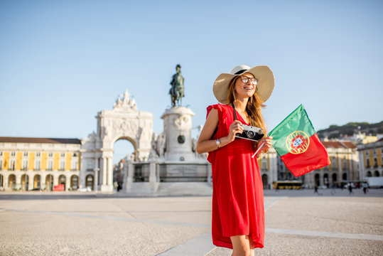 Lifestyle portrait of a young woman tourist with portuguese flag standing on the main square during the morning light in Lisbon city, Portugal