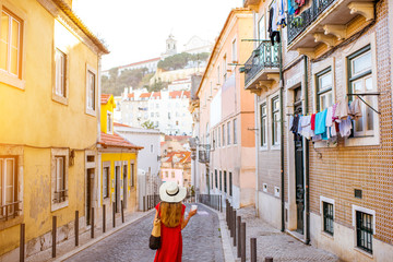 Woman tourist walking back on the narrow street in Alfama region during the morning light in...