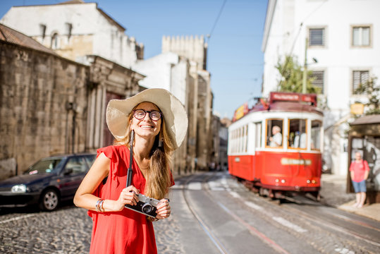 Portrait of a young woman traveler in red dress standing on the street with famous tourist tram on the background in Lisbon, Portugal