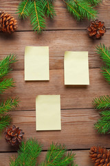 Christmas frame with stickers for notes, with spruce branches and cones on a natural wooden background.