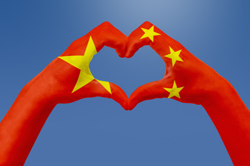 Hands flag of China, shape a heart. Concept of country symbol, on blue sky.