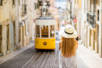 Young woman tourist photographing famous retro yellow tram on the street in Lisbon city, Portugal