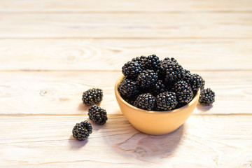 Close up of ripe blackberries in a white ceramic bowl over rustic wooden background