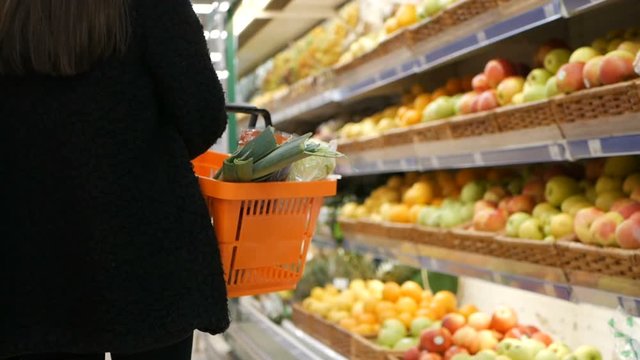 Slow motion of a woman with shopping cart walking alongin the supermarket. Buying fruit