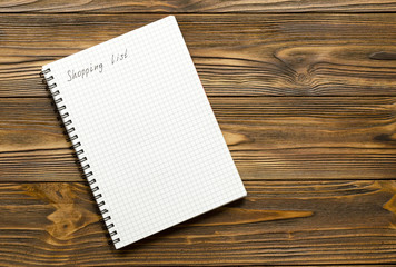 shopping list phrase in notepad on brown wood table 