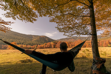 man lies in hammock in woods.